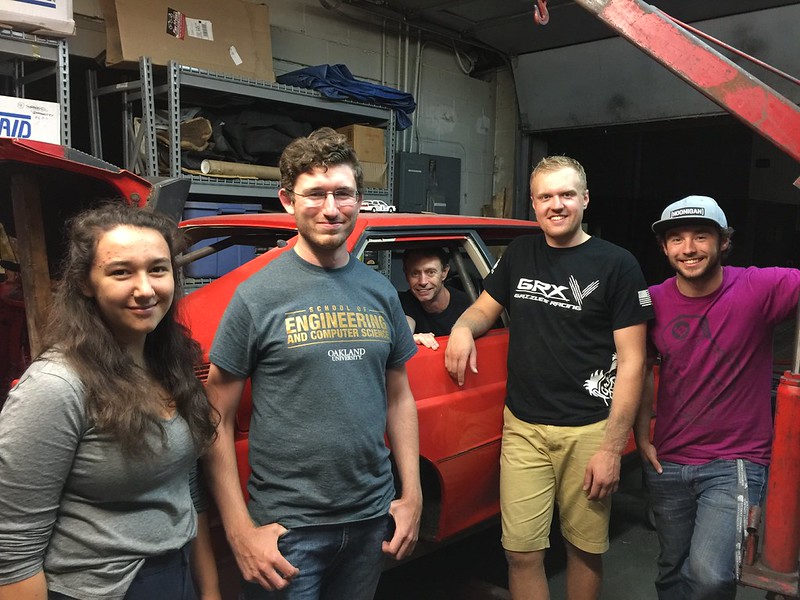 29073938883_eb60c9b774_c Five young adults posing around a red car inside a garage or workshop