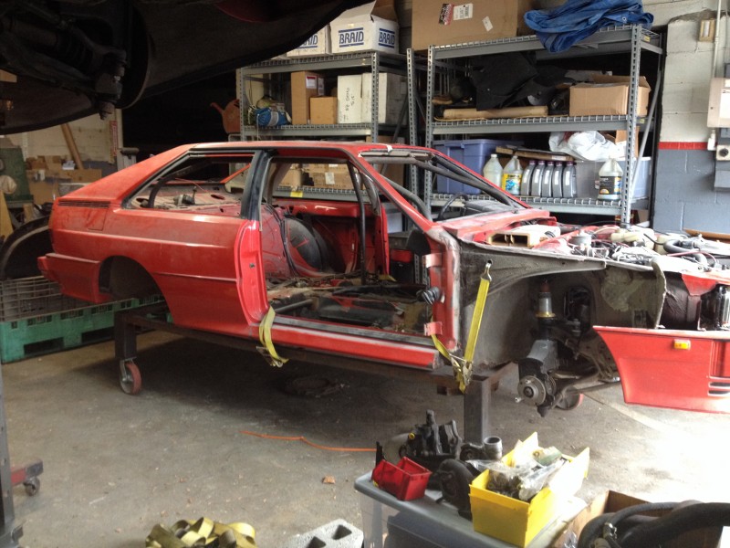 29594504181_05cbdb5f74_c Partially disassembled red car body in a garage with missing wheels and interior components