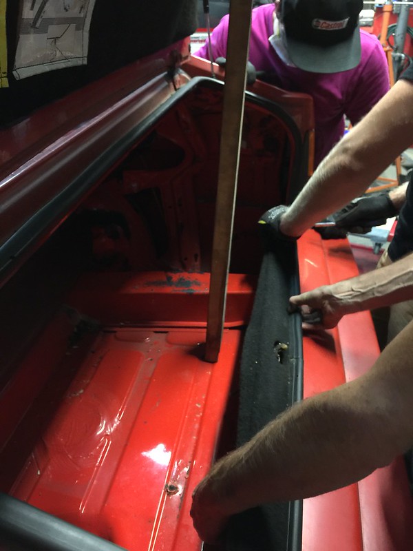 29663020296_a58890af1a_c Two people working on removing or installing a black fabric lining inside the trunk of a red vehicle