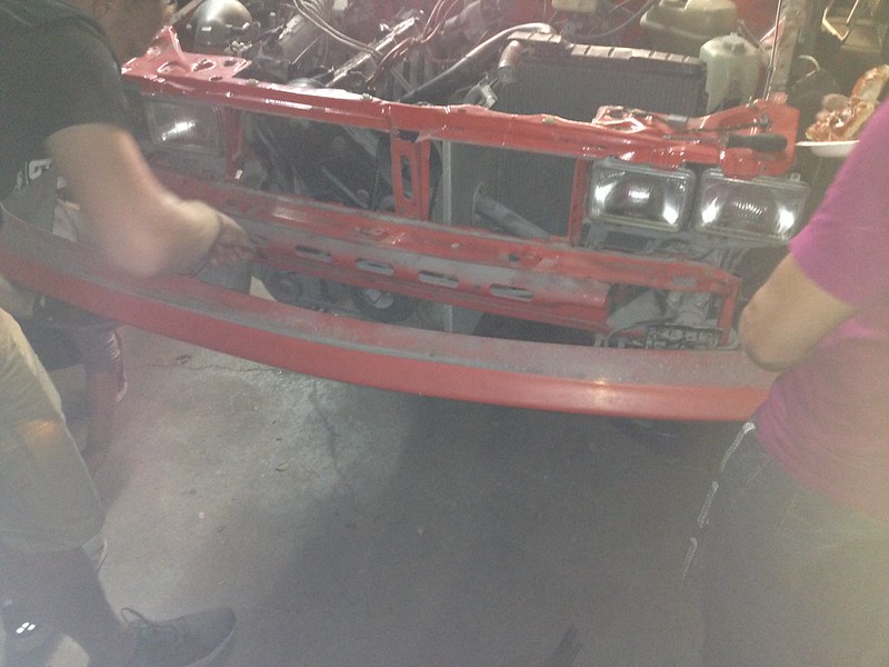 29702765415_0c61c32fac_c Two people installing a red front bumper on a car without the grille and headlights