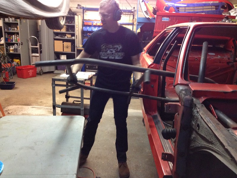 29709879040_aa8f1b47b9_c A person wearing headphones holding a metal frame near a red car chassis inside a workshop