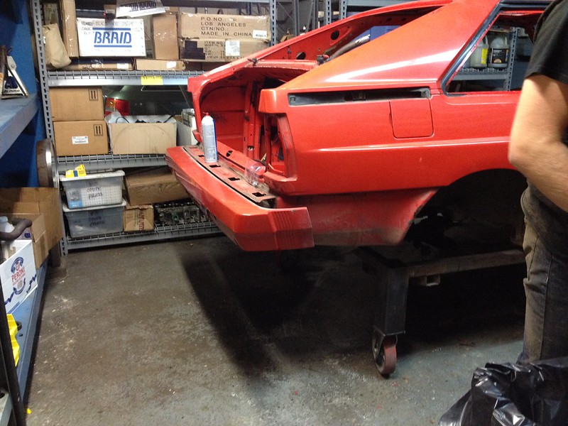 29920728761_f0d188fdc2_c Rear end of a red car undergoing restoration in a garage with shelves of boxes