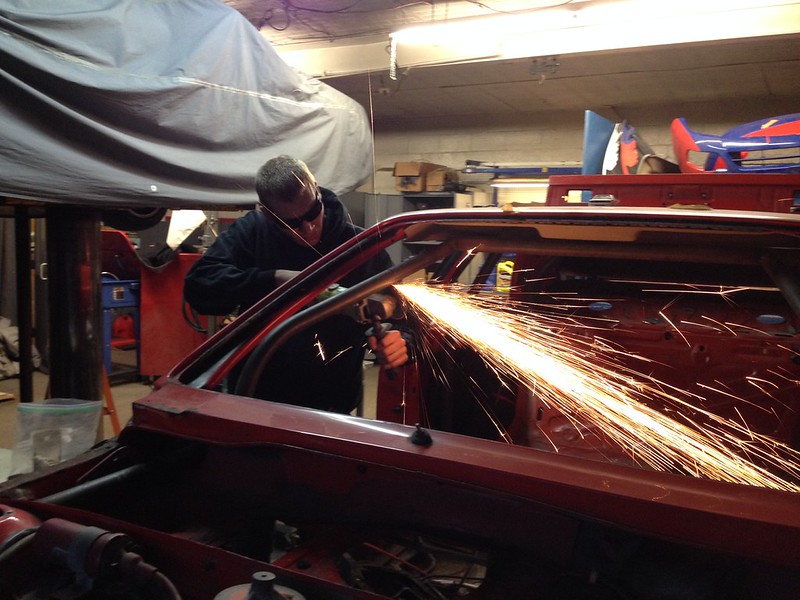29969724616_0caf2f70ef_c A person wearing safety goggles using a power tool to grind or cut metal on a car frame, producing sparks in a workshop