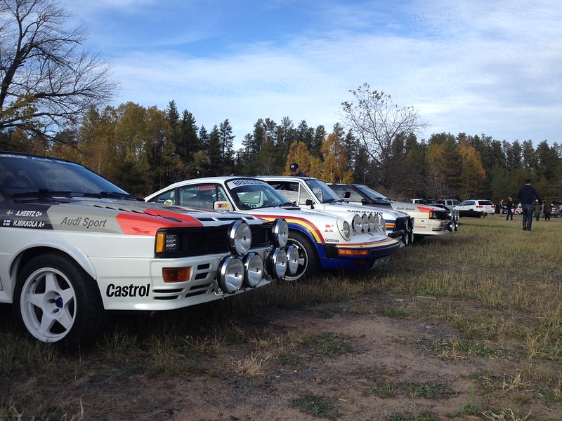 30377768686_90437e5fb4_c Row of classic Audi Sport rally cars parked on a grassy field during daytime with people in the background