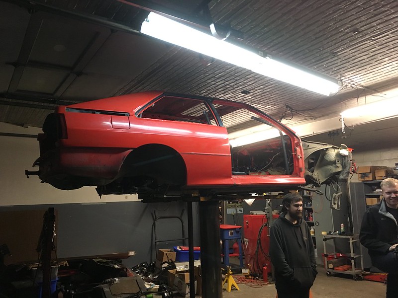 30450468060_da45bc2ba9_c Red car shell lifted on a hydraulic lift inside a garage with two men nearby