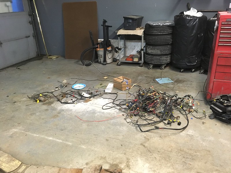 31426518334_d9615480d8_c Disassembled vehicle wiring harnesses spread out on a garage floor with stacked tires, tools, and equipment in the background