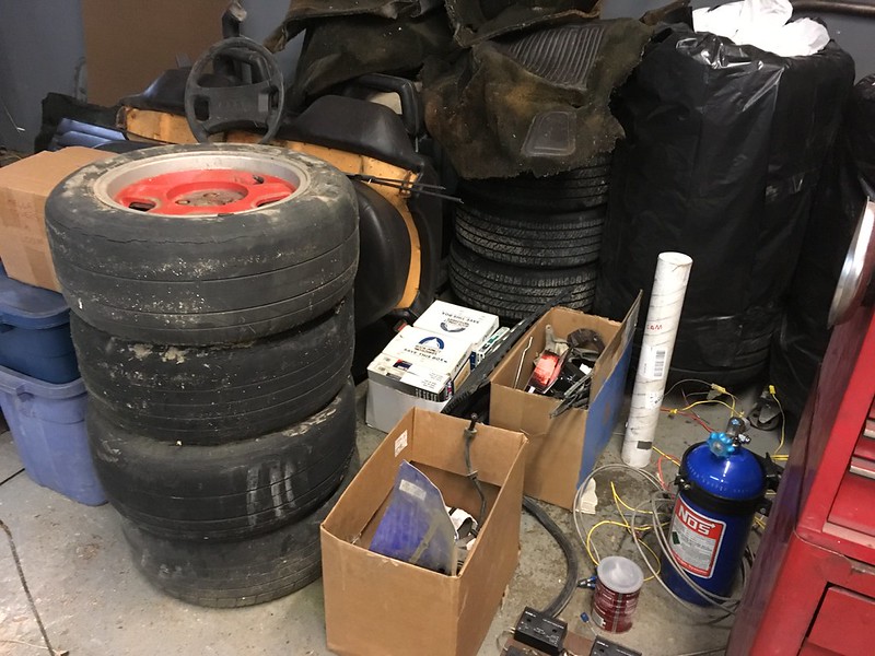 Stack of used car tires, cardboard boxes filled with car parts, and a blue NOS nitrous oxide tank in a garage