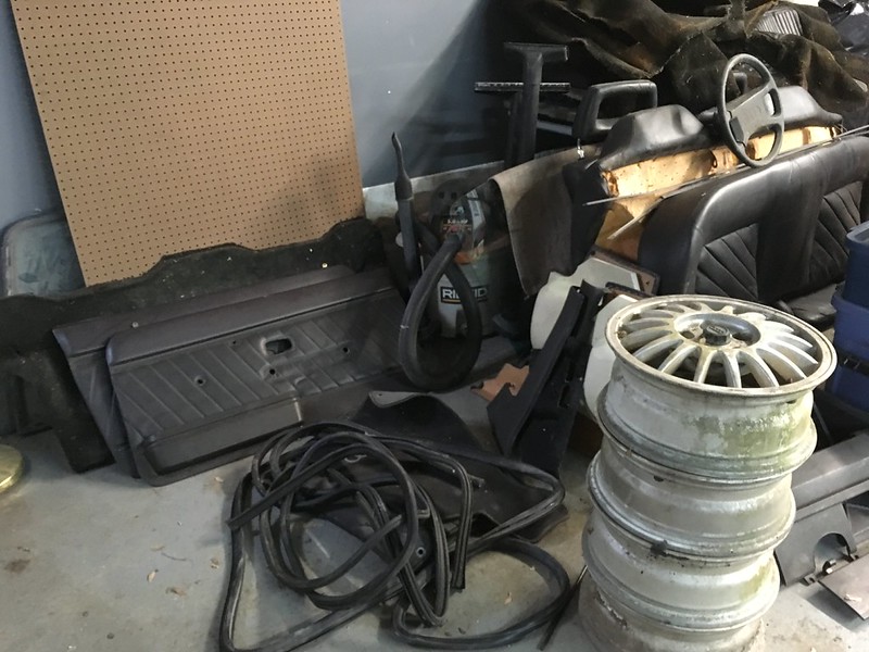 Stack of three old car rims beside coiled rubber hoses and black car door panels in a garage