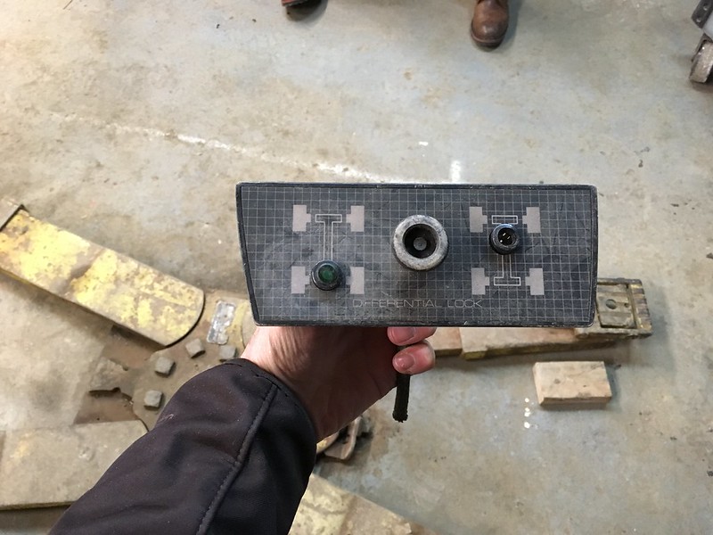 Hand holding a UR Quattro differential lock control panel with buttons and a knob, showing axle and drivetrain diagrams on a workshop floor