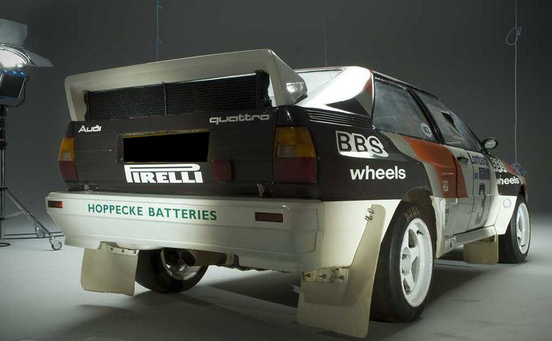 Rear view of an Audi Quattro rally car featuring Pirelli branding and BBS wheels, set against a neutral background.