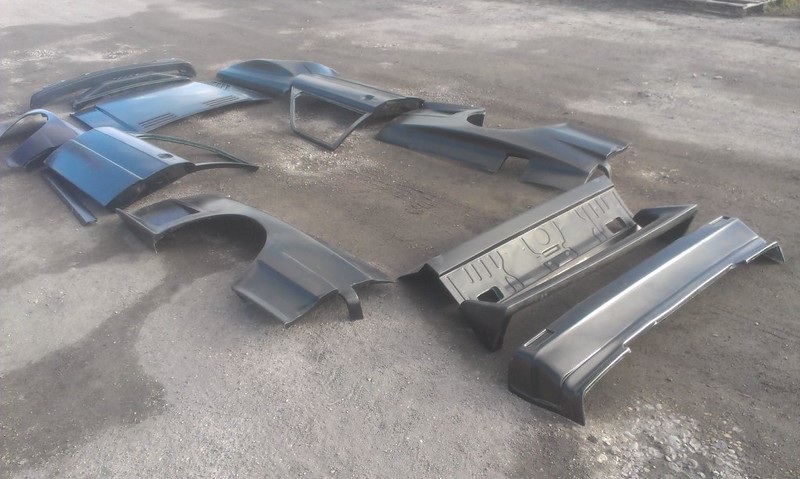 Various black automotive body panels arranged on a gravel surface.