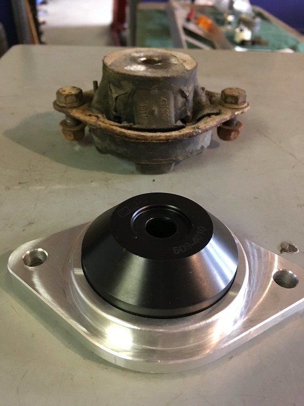 A comparison of two UR Quattro motor mounts, one new and shiny with a black top and silver base, and the other old and worn with rust on the metal parts.