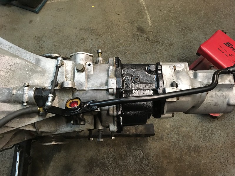 Close-up view of a UR Quattro transmission assembly with various components, including a black housing and connected pipes, placed on a workshop floor.