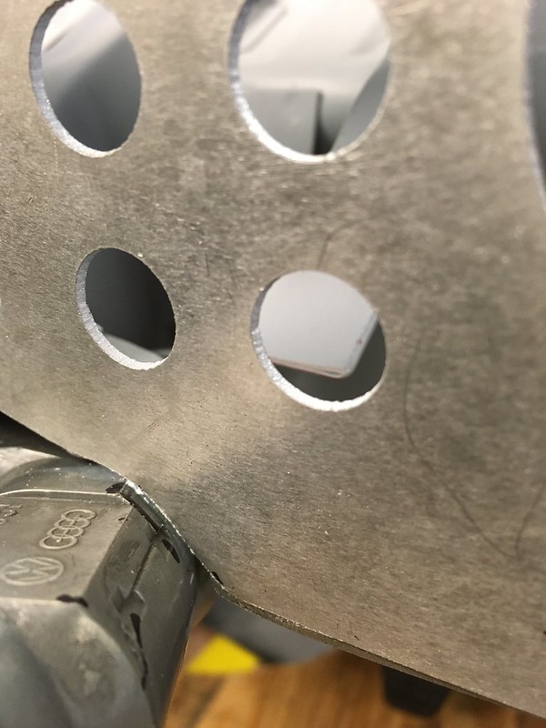 Close-up of a metal plate with several round holes, showing part of a black object beneath it.