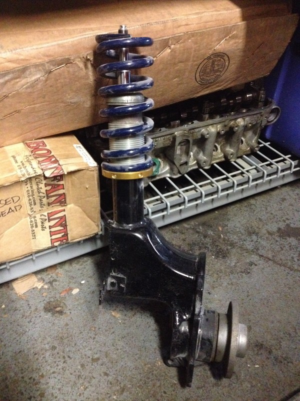 A black UR Quattro rally suspension strut with a blue coil spring, positioned on a storage rack next to boxes and other automotive components.