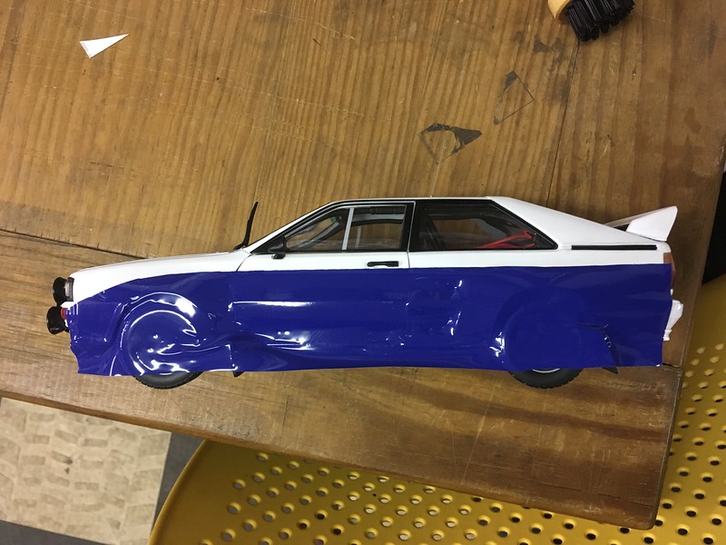 A white and blue model UR Quattro with tape covering the wheels and lower body, placed on a wooden surface