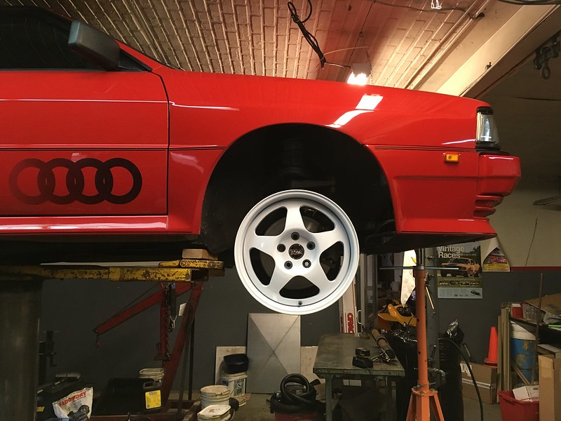 Red UR Quattro with Audi logo on side left front wheel removed in a garage workshop