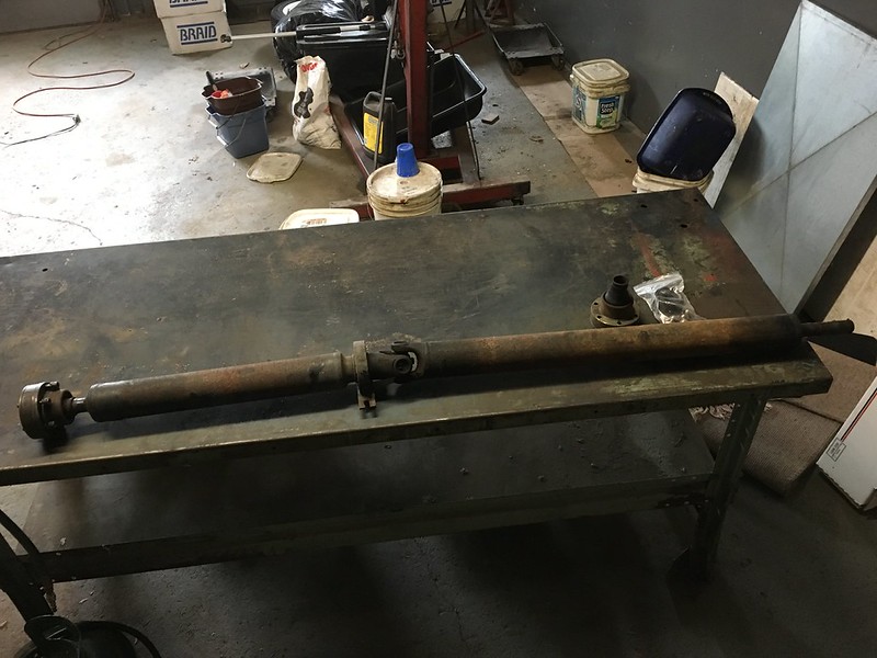 33574197792_08d24c8d94_c Rusty driveshaft lying on a metal workbench in a garage with tools and buckets in the background