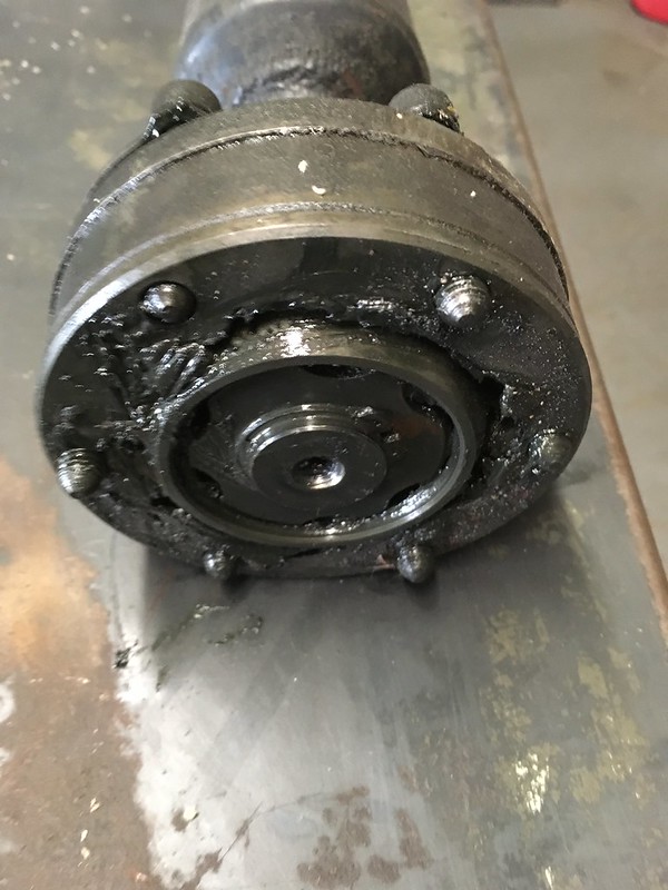 Close-up view of a dirty, greasy mechanical component, showing a circular part with bolts and a central shaft.
