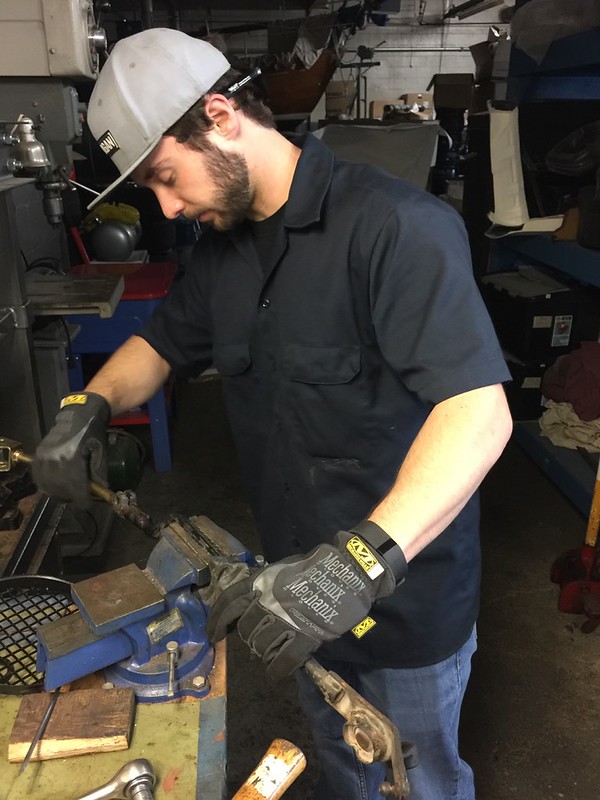 33971025716_a68656352f_c A person wearing a gray cap and black shirt working with a blue bench vise in a workshop