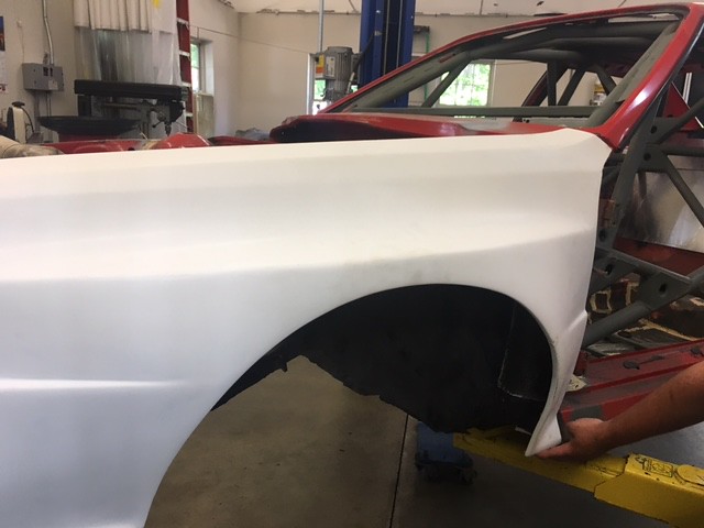 Close-up of a white car body panel in a workshop, revealing part of an unfinished vehicle with a red interior.