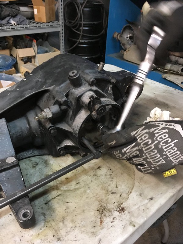 A mechanic using a ratchet on a disassembled gearbox on a workbench, surrounded by tools and parts.