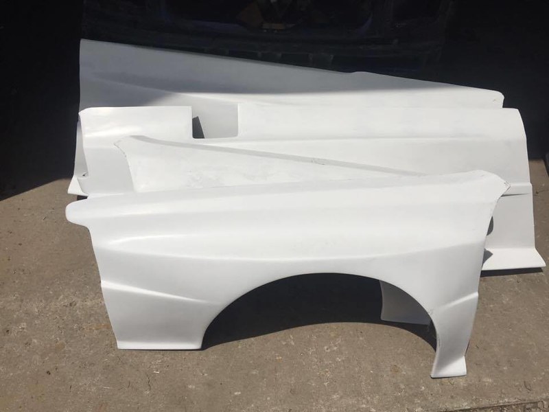 Several white car body panels arranged on a concrete surface.