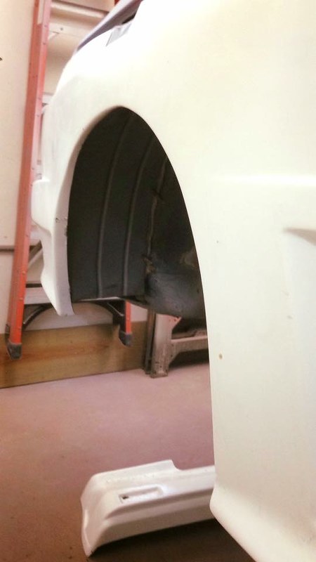 A close-up view of a UR Quattro's wheel arch, showing the inner structure and some parts of the vehicle, with a ladder and workshop background.