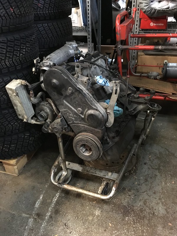 A UR Quattro engine on a metal cart, with blue rags nearby and stacked tires in the background.
