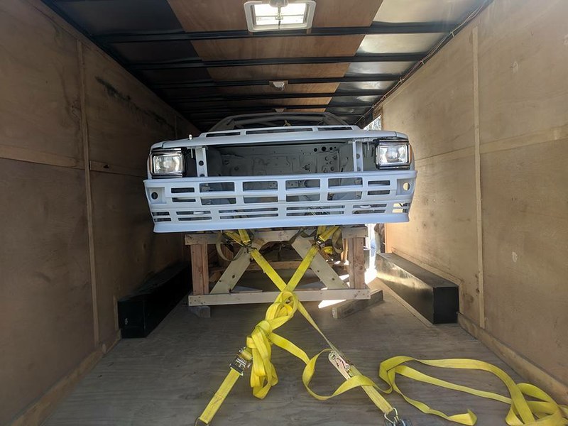 A UR Quattro chassis secured with yellow straps inside a trailer, shown from the front with a blank white exterior.