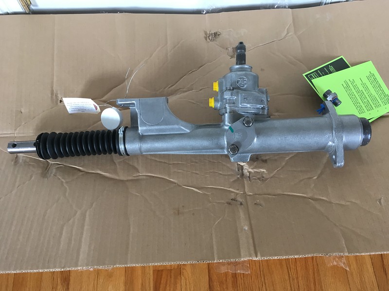 A new UR Quattro steering rack assembly placed on a cardboard surface, featuring a metallic finish and various connection points, with a packaging tag visible.