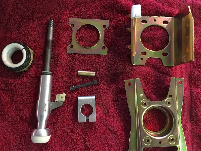 An assortment of mechanical parts including a lever, several brackets, a metal cylinder, and other components, arranged on a red towel.