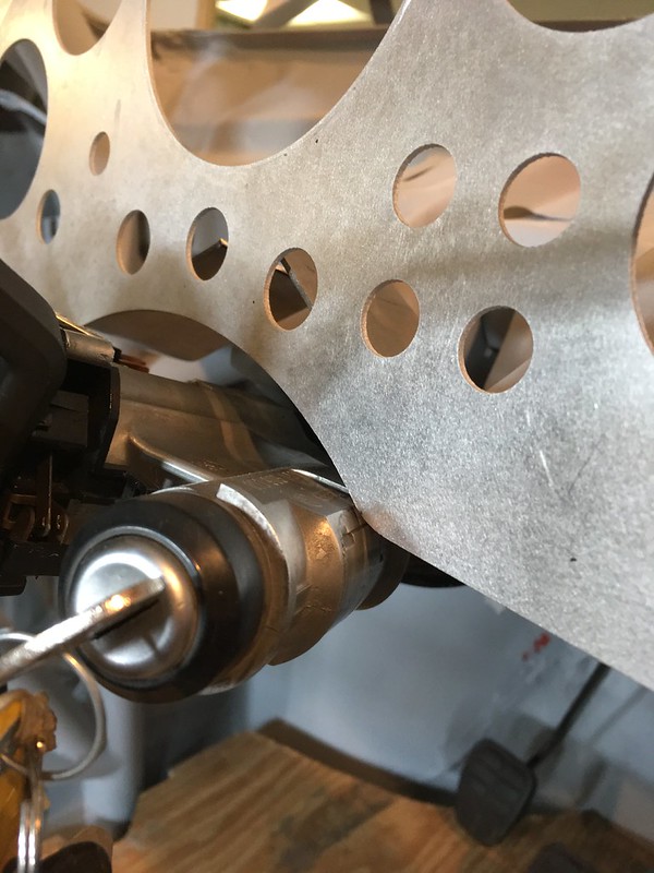 Close-up view of a metallic component with several circular holes, displaying a mechanical device and part of a key near a wooden surface.