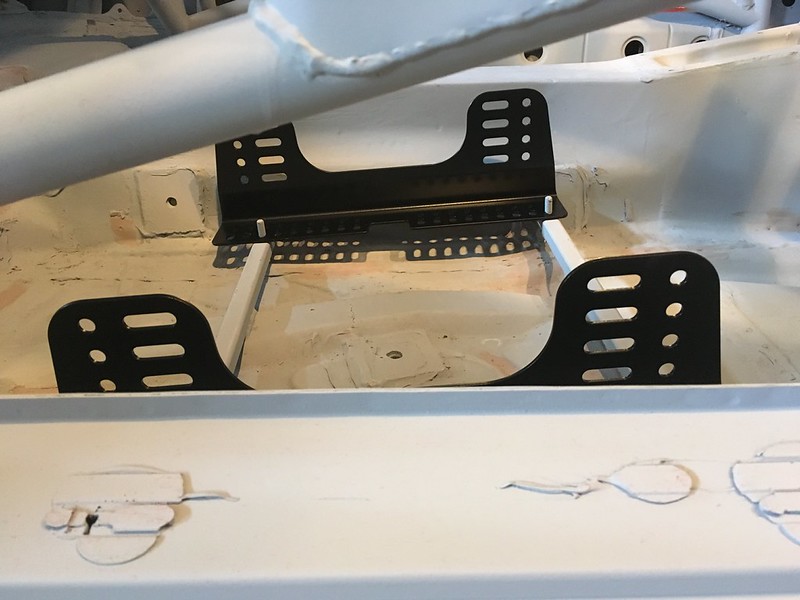 Close-up view of a black metal seat bracket installed in a UR Quattro interior, showing the surrounding white floor and mounting points.