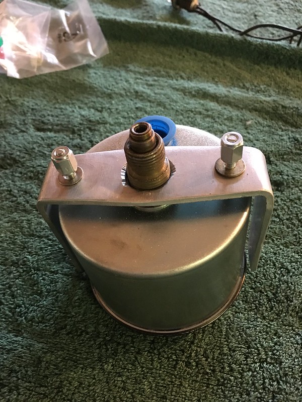 Close-up of a cylindrical metallic fuel filter with a bracket and connection fittings, resting on a green textured surface.