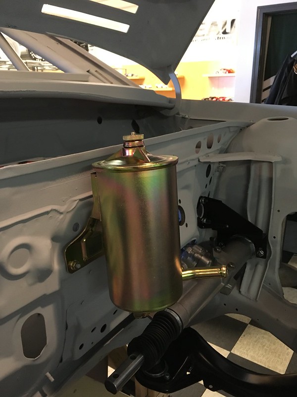 Close-up of a metallic fuel filter mounted in a car chassis, showcasing its shiny finish and connection points.