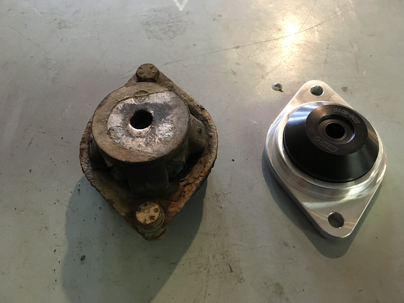 Comparison of an old, worn-out UR Quattro engine mount on the left and a new performance engine mount on the right, placed on a gray surface.