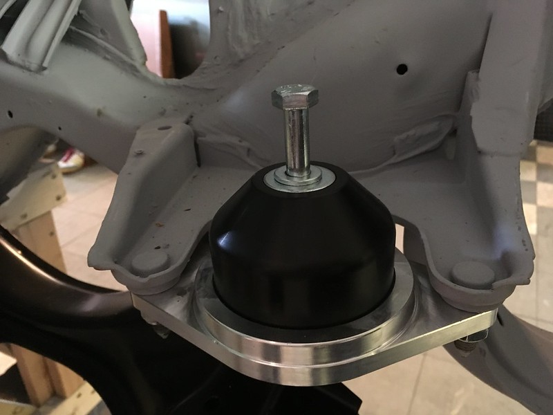 Close-up of a black rubber engine mount secured to a metallic base with a silver hex nut, part of a vehicle chassis.