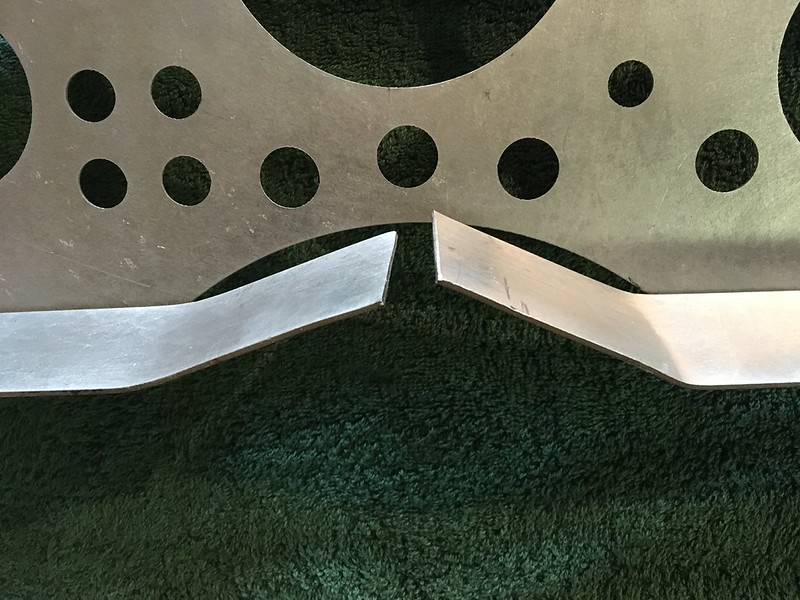 A close-up view of two metal components with angled edges, showcasing different shapes and surface finishes, set against a green fabric background.