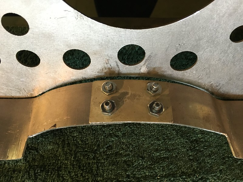 Close-up view of a metal component with circular holes and attached bolts on a surface.