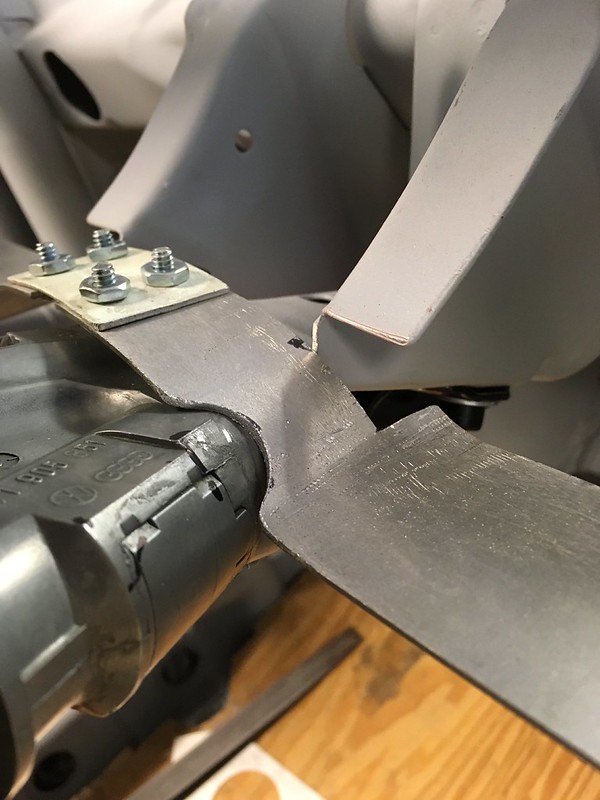 Close-up of a metallic component featuring bolts and a curved piece, showcasing part of a mechanical assembly on a wooden surface.