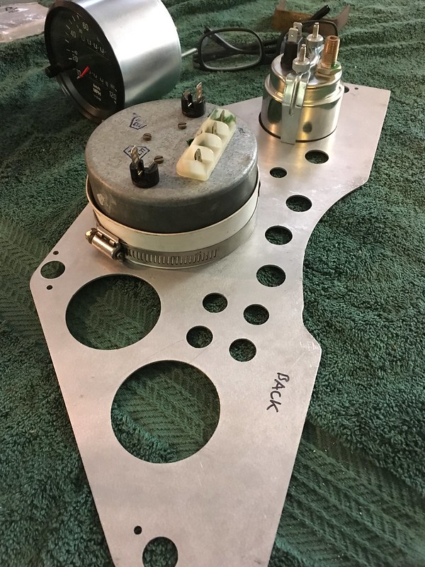 Close-up of UR Quattro rally dashboard components including a metal backing plate with several holes, a gauge, and electrical connections on a green towel.
