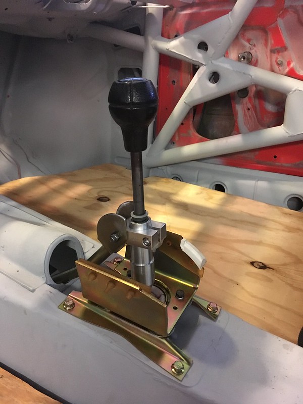 A close-up view of a manual gear shifter installed in a vehicle's interior, featuring a black knob and metallic base mounted on a wooden surface.