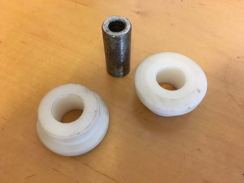 Two white plastic washers and a metal cylindrical spacer on a wooden surface.