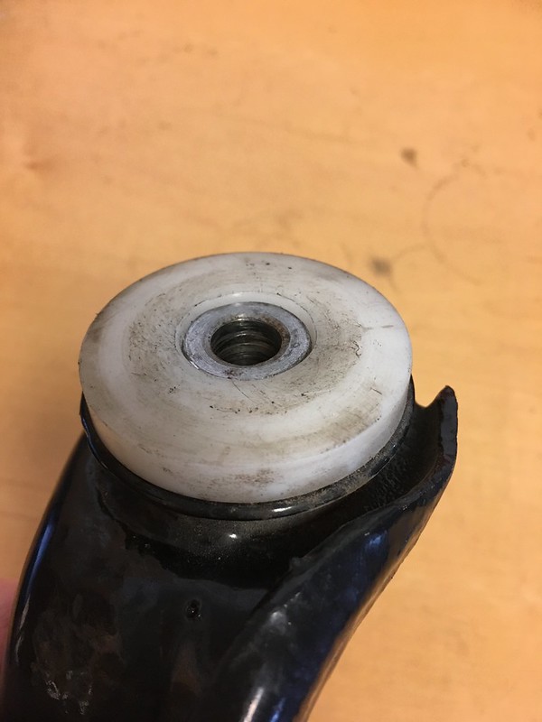 Close-up of a black mechanical part with a white circular component at the top, featuring a central threaded hole.