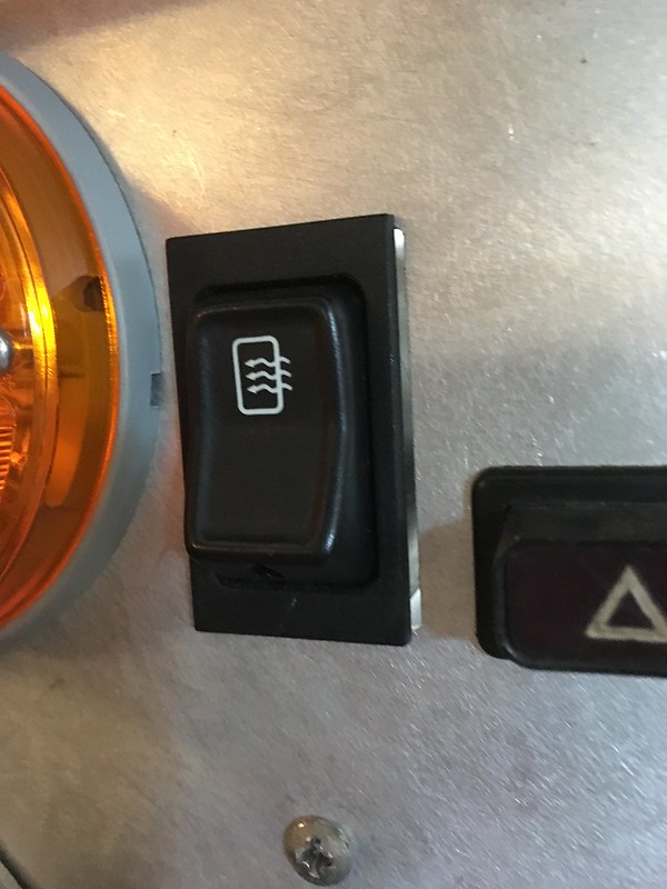 Close-up of a UR Quattro rally switch with a symbol for heated mirrors, located next to an orange indicator light and a hazard button.